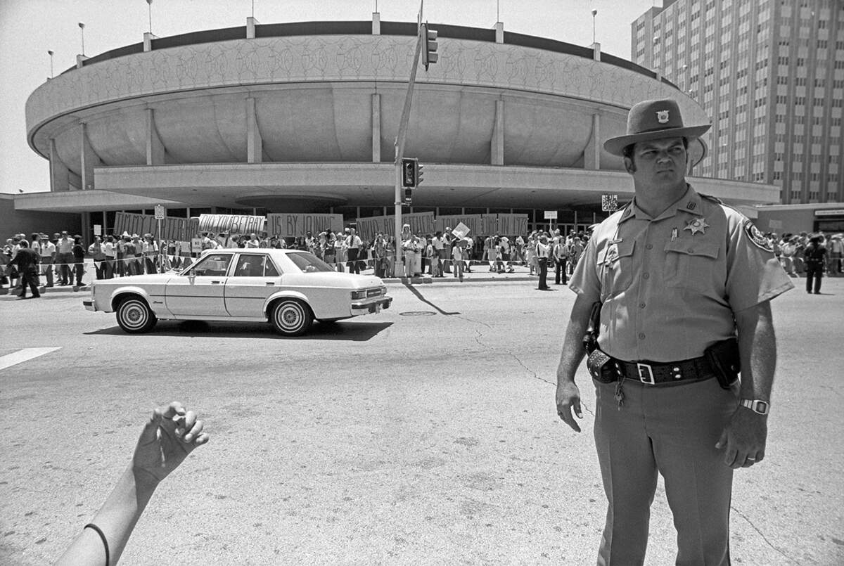 A law enforcement officer is seen stationed outside of the Tarrant County Convention Center in downtown Fort Worth ahead of President Jimmy Carter’s arrival for a luncheon on June 23, 1978. The group seen behind the officer appears to be protesting Carter’s visit, holding signs calling for his impeachment and a string of signs reading “Jimmy Carter Why Did You Betray Us By Joining David Rockefeller’s Trilateral Comm (Commission) In 1973.”