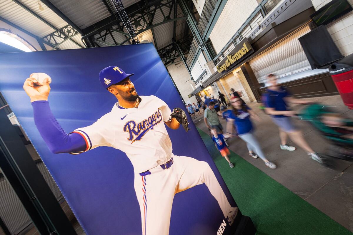 Fans walk by the poster of Texas Rangers infielder Marcus Semien during the first day of the 2024 MLB All-Star Village at Choctaw Stadium in Arlington on Saturday, July 13, 2024.