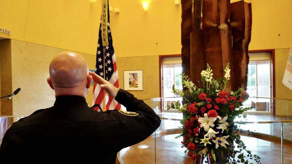 Fort Worth Police Chief Neil Noakes salutes the American flag standing in front of a bent steel beam from the World Trade Center North Tower. The beam is displayed at the entrance of the Fort Worth Museum of Science and History.