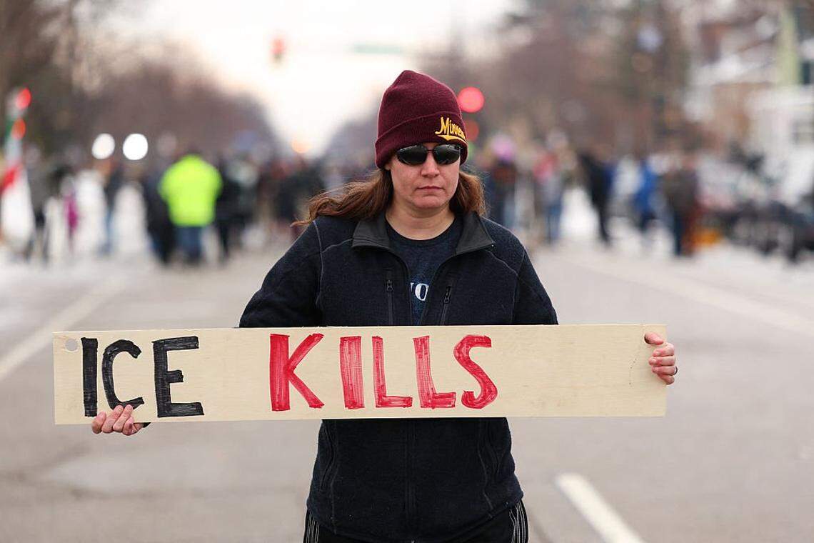 A woman holds a sign reading "ICE kills" while standing in the street where 37-year-old Renee Nicole Good was shot and killed at point blank range on January 7 by a US Immigration and Customs Enforcement (ICE) agent as she apparently tried to drive away from agents who were crowding around her car, in Minneapolis, Minnesota, on January 8, 2026. A US Immigration and Customs Enforcement (ICE) agent shot and killed an American woman on the streets of Minneapolis January 7, leading to huge protests and outrage from local leaders who rejected White House claims she was a domestic terrorist. (Photo by CHARLY TRIBALLEAU / AFP via Getty Images)