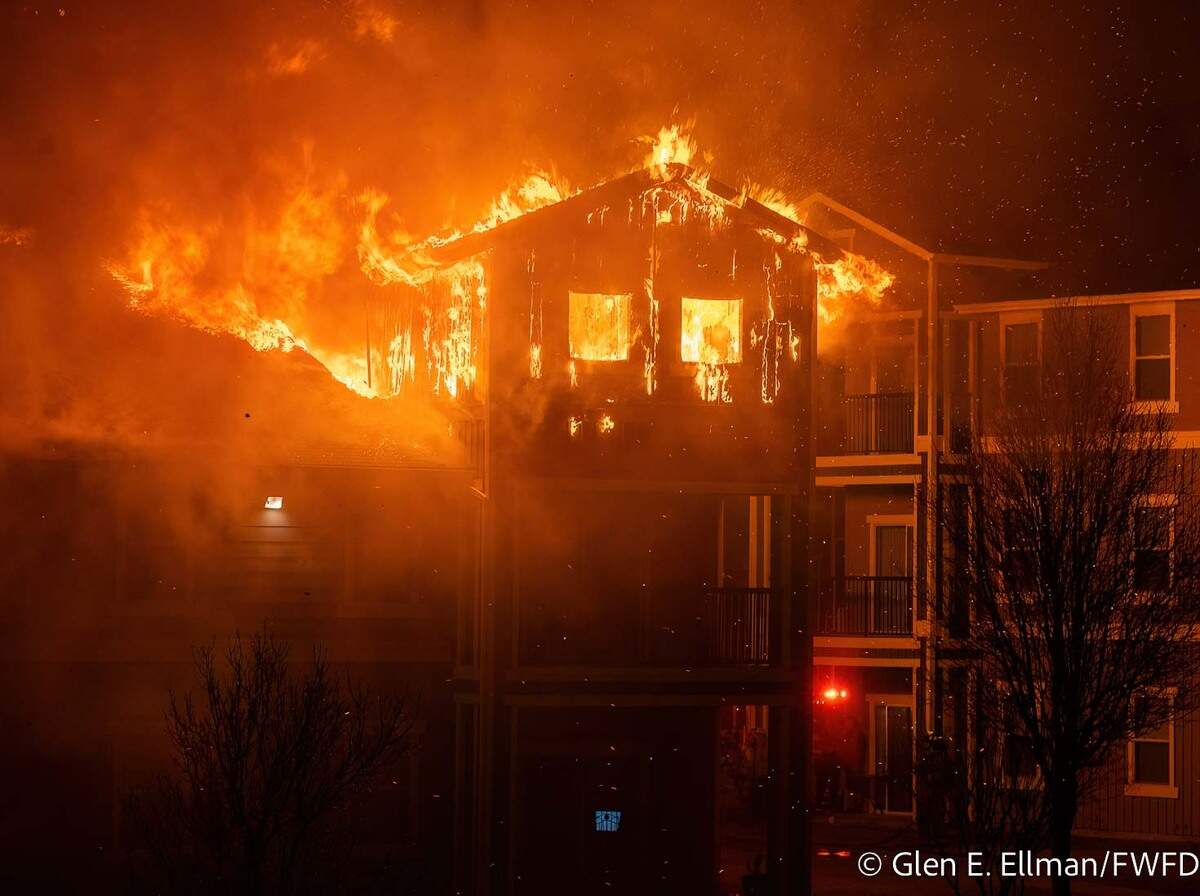 Orange flames and smoke come out the top of an apartment building.
