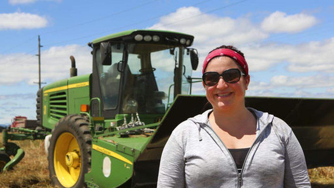 In this Thursday June 21, 2018 photo, fifth generation farmer Marie Bowers stands in front of her grass cutter machine on her family’s farm in Coburg, Ore.  Increasingly, U.S. farmers need access to high-speed internet and technology to compete globally.