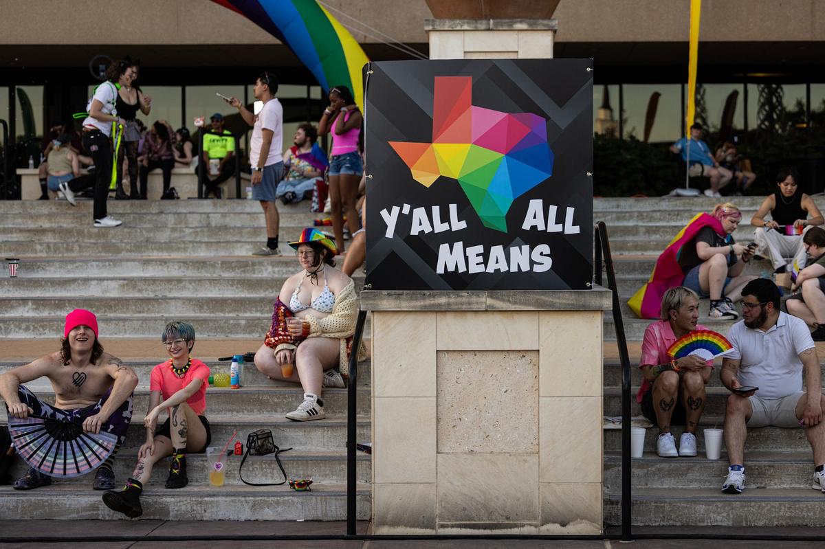 Event attendees rest in the shade away from the heat next to a Pride sign saying “Y’all Means All” at the Arlington Pride event at Levitt Pavilion in Arlington on Saturday, June 8, 2024.