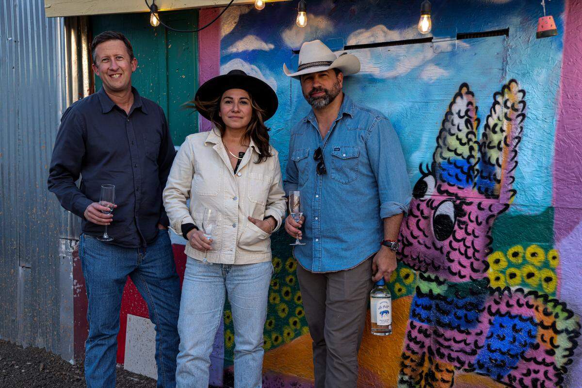 The three founders of La Pulga Spirits stand in front of a colorful mural.