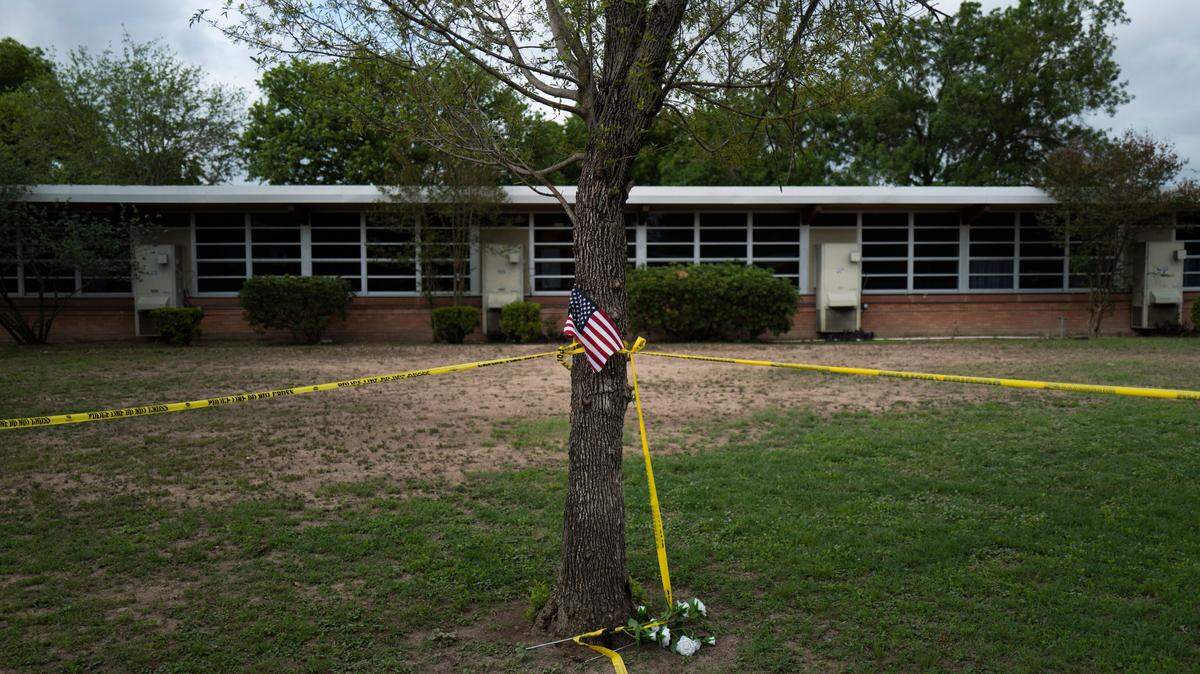 A school building stands behind a tree with an American flag and crime scene tape at Robb Elementary School in Uvalde, Texas on Monday, May 30, 2022. On May 24, an 18-year-old entered the school and fatally shot 19 children and two teachers.