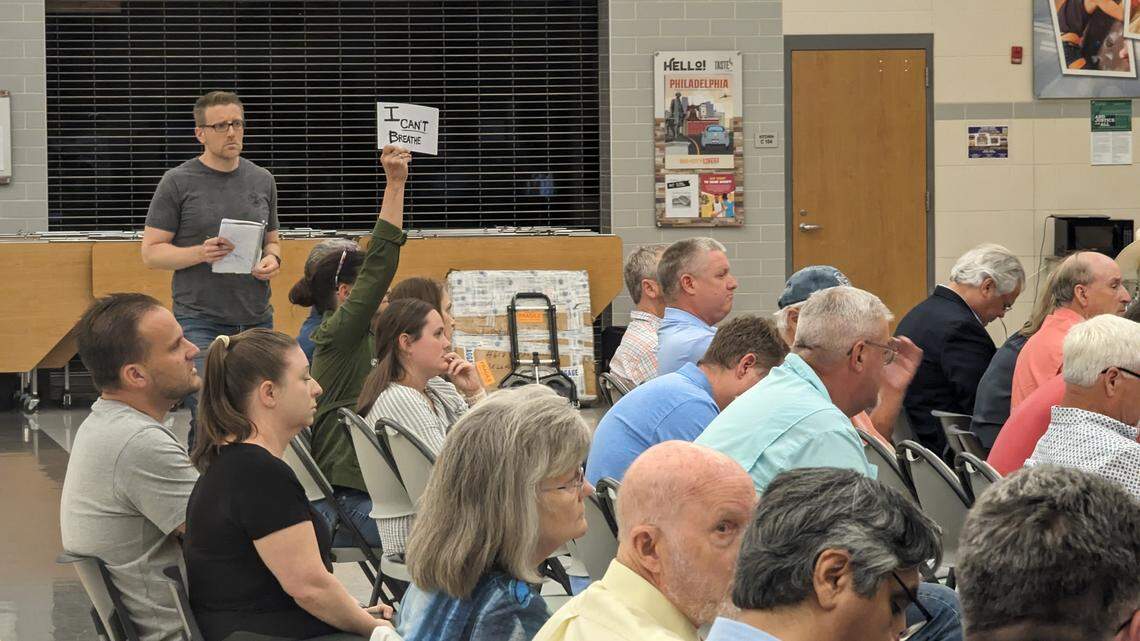 A woman sitting among others in a high school cafeteria holds up a sign reading "I can't breath."