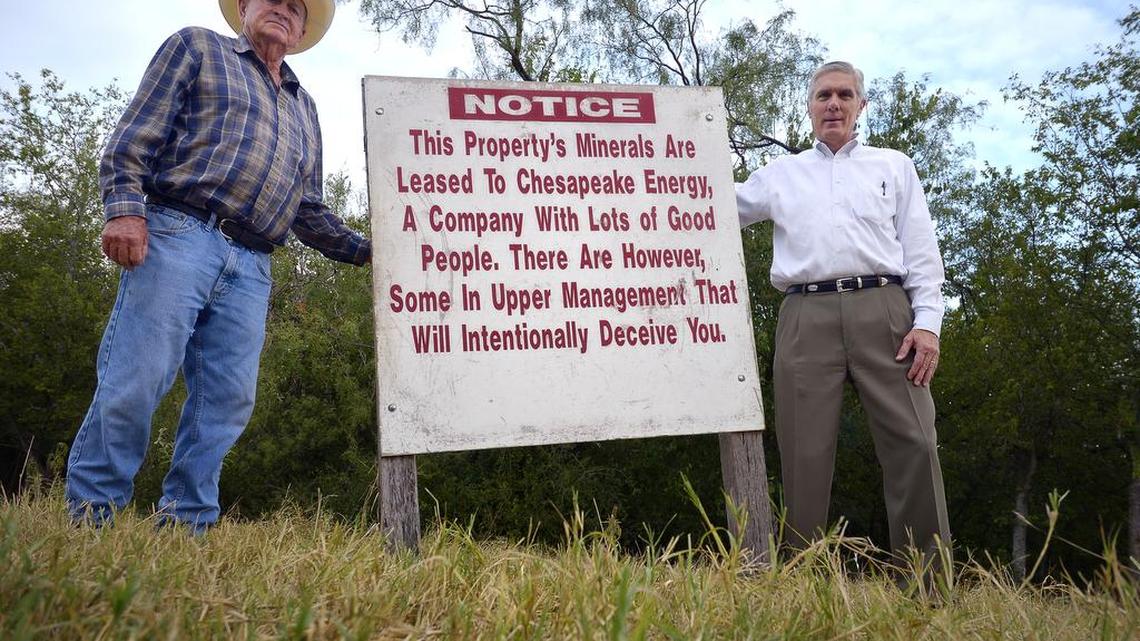 Weldon Wadsworth, left, and Lem Miller stand next to a sign on Wadsworth’s property in Joshua. They are among attorney Dan McDonald’s clients who claim they’ve been underpaid royalties.