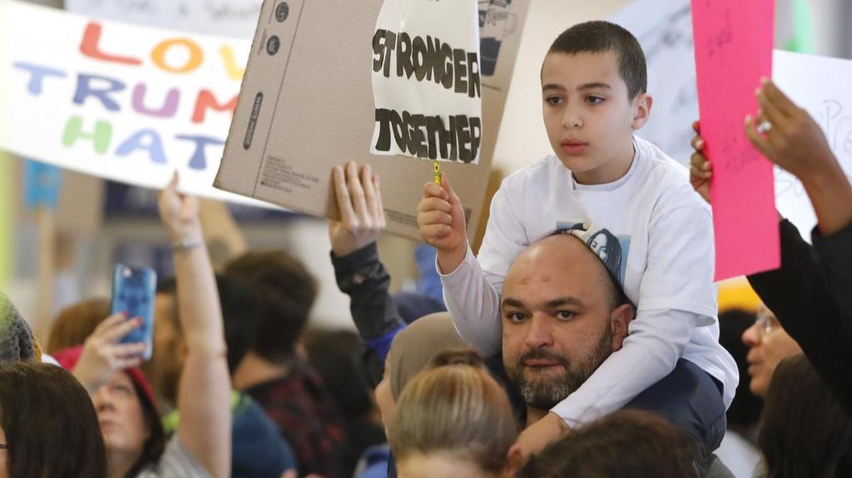 Hazem Elsharkawi holds his son Adam, 8, on his shoulders as they show support for travelers detained at DFW Airport on Sunday. More than 800 people protested Trump’s order that temporarily bans citizens of seven predominantly Muslim nations from entering the U.S.