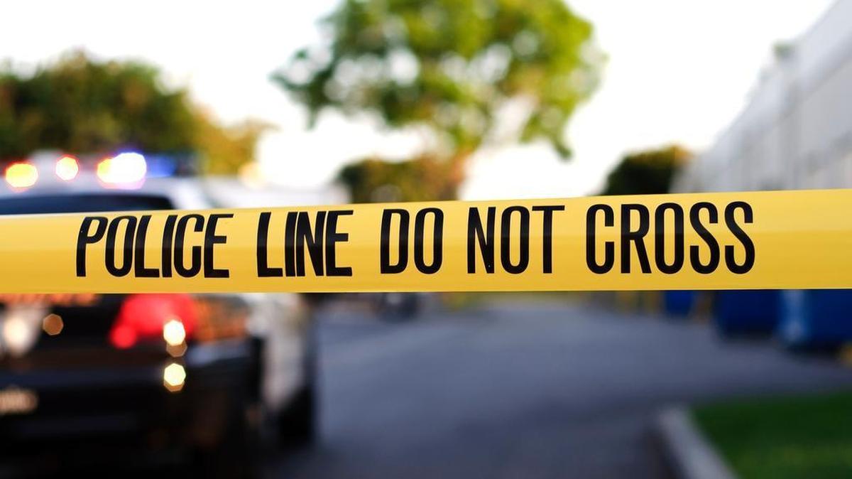 A blurred police car is in the background behind yellow crime scene tape.