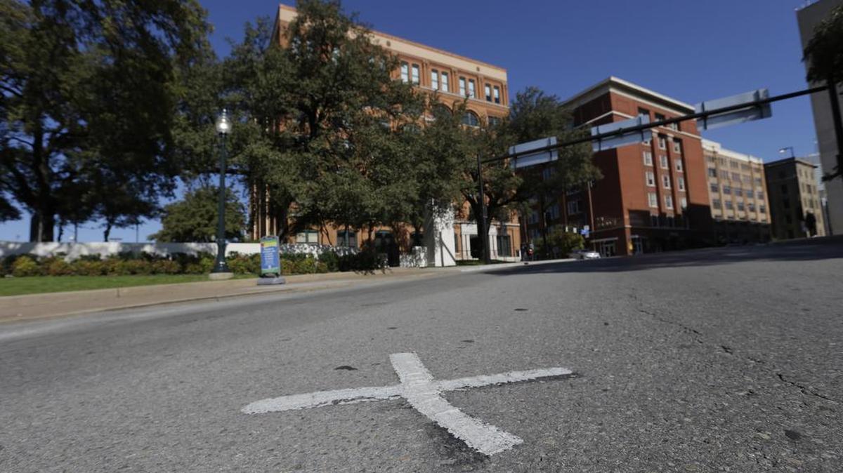 In this Nov. 12, 2013 file photo, an X marks the spot on Elm Street where the first bullet hit President John F. Kennedy on Nov. 22, 1963 near the former Texas School Book Depository, now known as the Sixth Floor Museum, background, on Dealey Plaza in Dallas. The Xs on the street are gone.