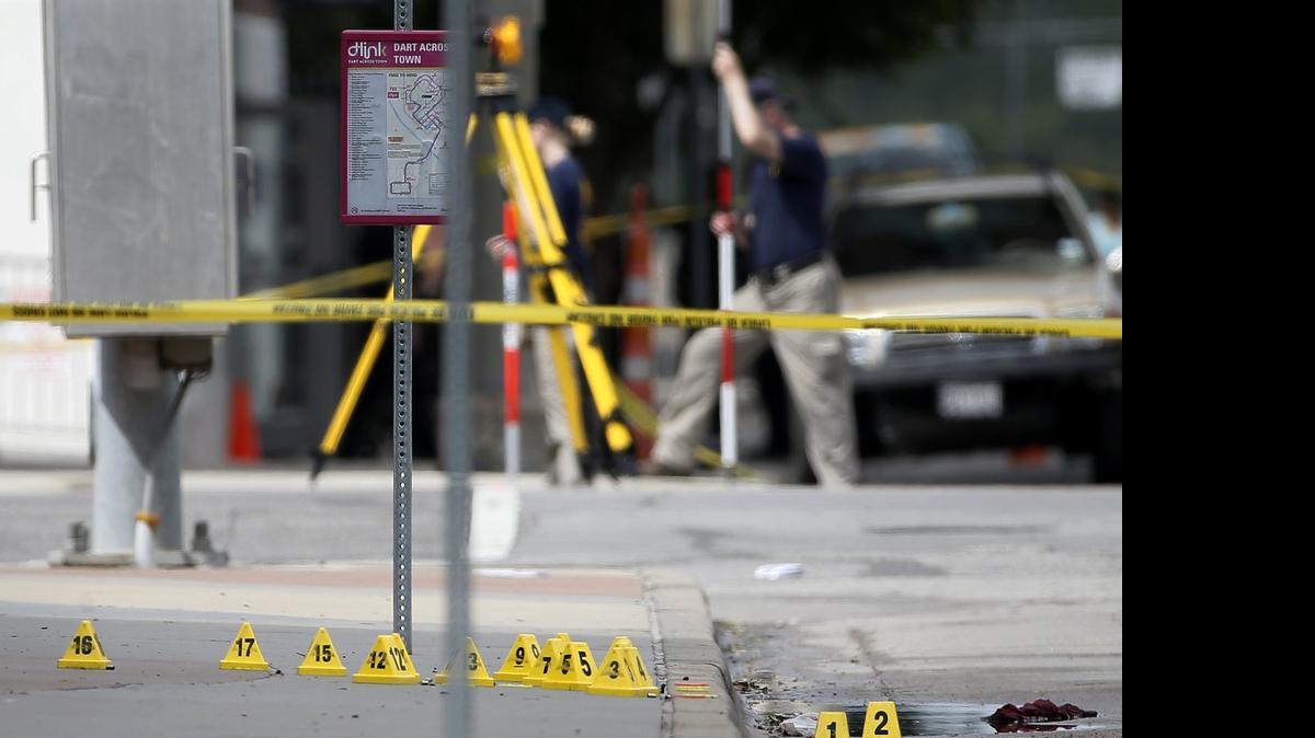 
Evidence markers on seen on a sidewalk in front of Dallas police headquarters as members of the FBI evidence response team, rear, investigate an intersection in front of the building Saturday June 13, 2015, in Dallas. A police sniper shot a cornered suspect in an overnight attack on the Dallas Police Department's headquarters, and authorities were checking Saturday to see if he was alive or dead. (AP Photo/Tony Gutierrez)
