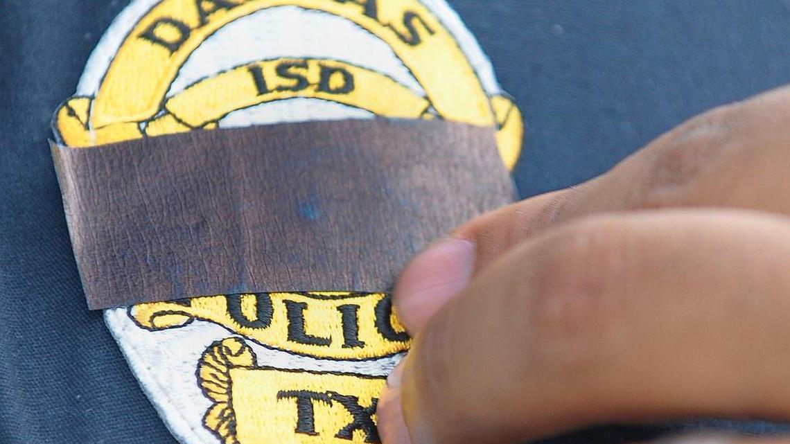 A Dallas ISD police officer adjusts a black tape over his badge in Dallas on Friday, the day after five officers were killed.
