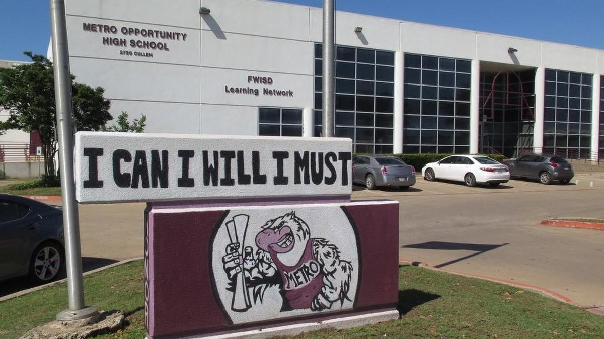 A sign reading "I can, I will, I must" stands in front of a light gray school building exterior.