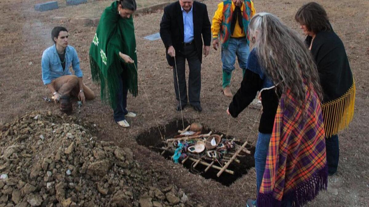 Officiants (from left: Austin Baker (son of Eddie Sandoval); Kui Red Eagle of Oklahoma; Jim Lane of Fort Worth; Eddie Sandoval; Mary Red Eagle of Oklahoma (plaid shawl) and Dana Austin of the Tarrant Co. Medical Examiner's office) lower the remains of a centuries-old Native American woman during a brief ceremony at Oakwood Cemetery in Fort Worth, Texas, on Thursday, December 21, 2017.