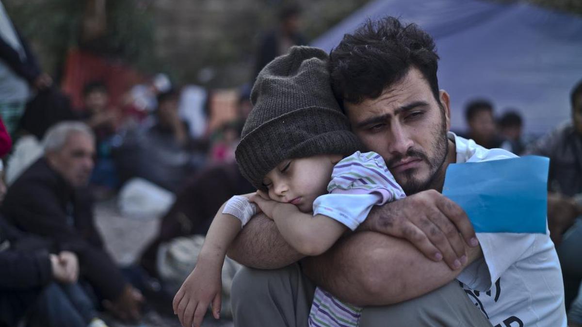 In this Oct. 4, 2015 file photo, a Syrian refugee child sleeps in his father's arms while waiting at a resting point to board a bus, after arriving on a dinghy from the Turkish coast to the northeastern Greek island of Lesbos.