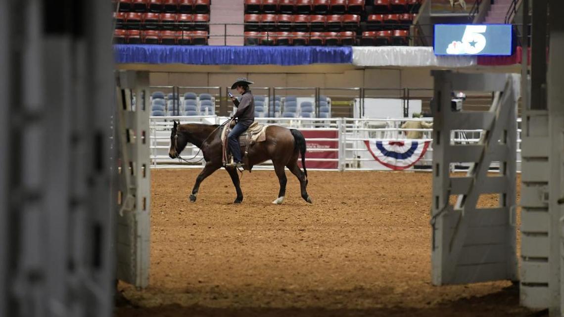 A rider checks his cell photo while warming up his horse inside Will Rogers Coliseum - the day before the Fort Worth Stock Show and Rodeo begins.