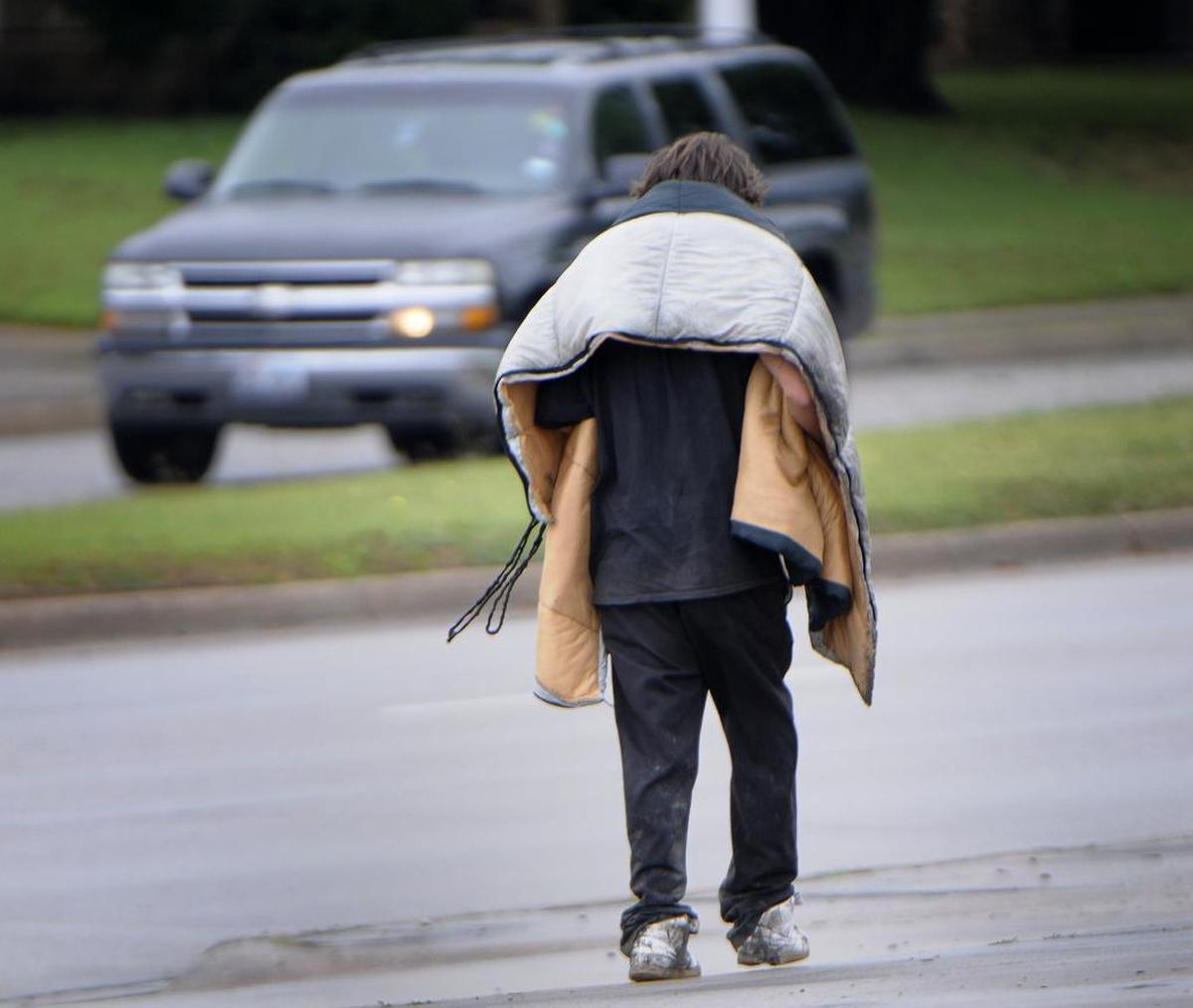 A pedestrian with a sleeping bag draped over his shoulders walks along Las Vegas Trail in Fort Worth.