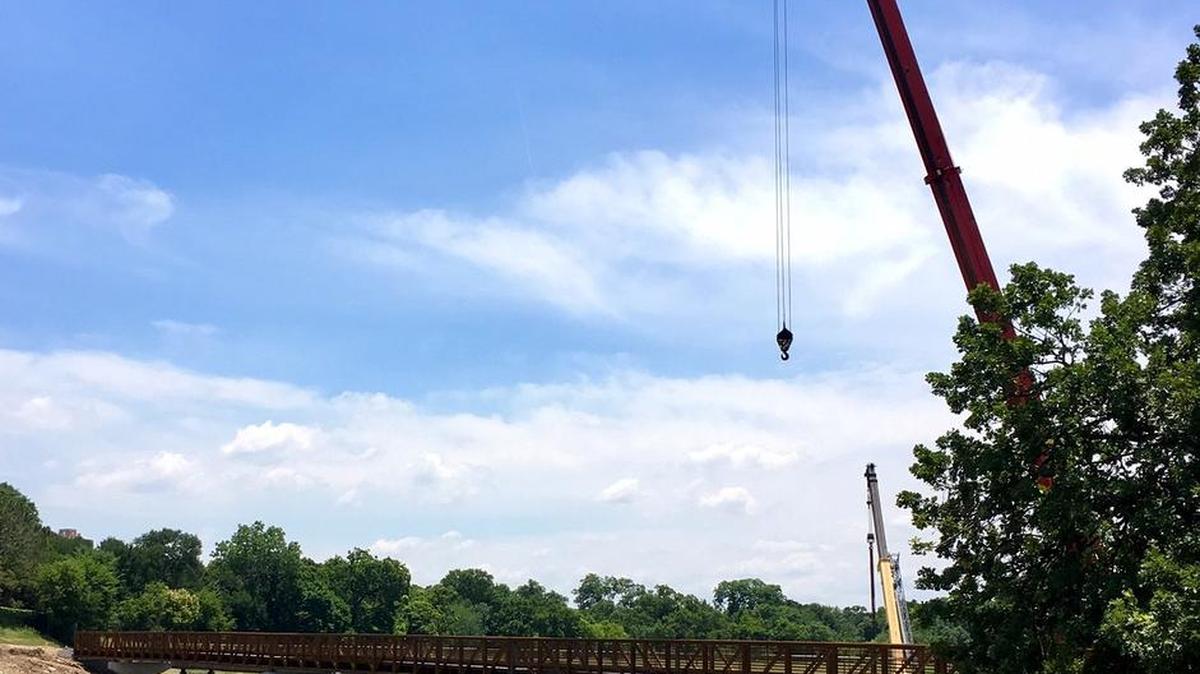 A crane is used to hoist the structural steel for a pedestrian bridge over the Trinity River near Mistletoe Heights and Old University Drive.