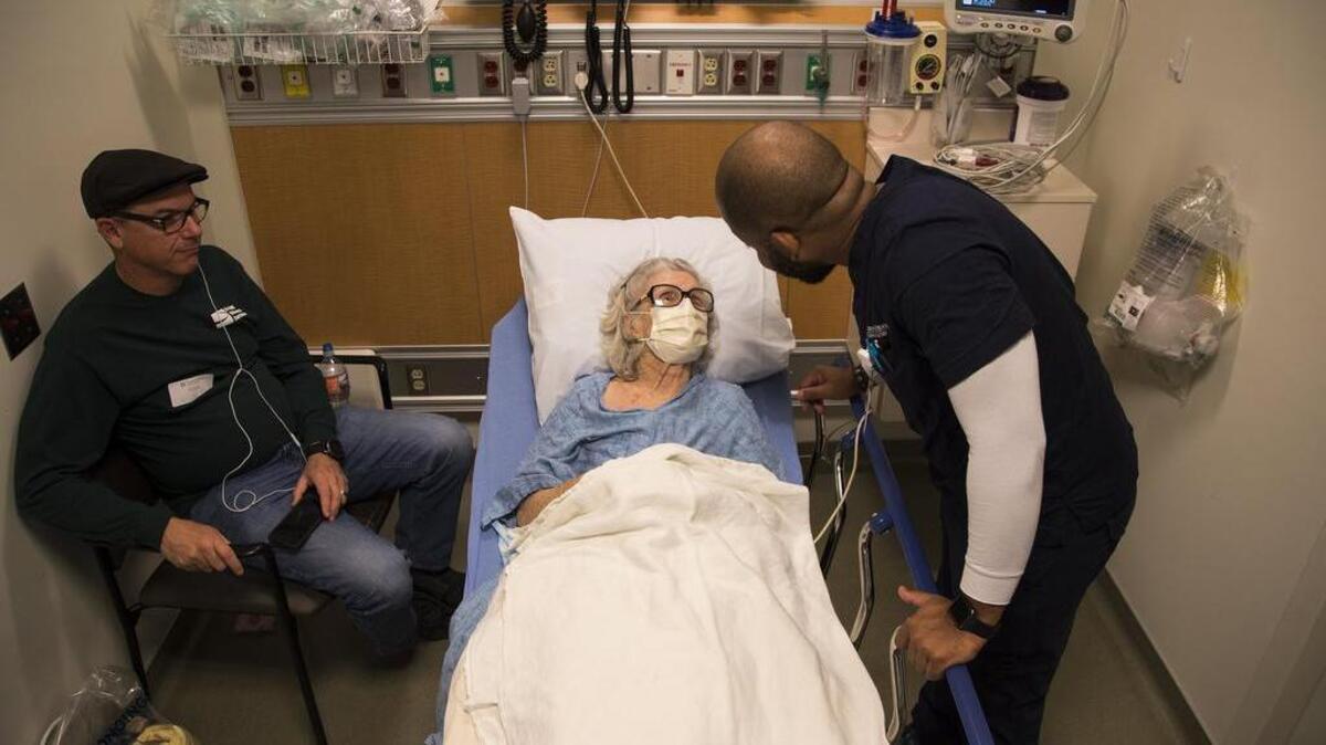 Nurse Reggie Withers tends to flu patient Louise Dominguez,84, as her son Al Dominguez, left, sits nearby inside the Emergency Room at Torrance Memorial Medical Center in Torrance, Calif.
