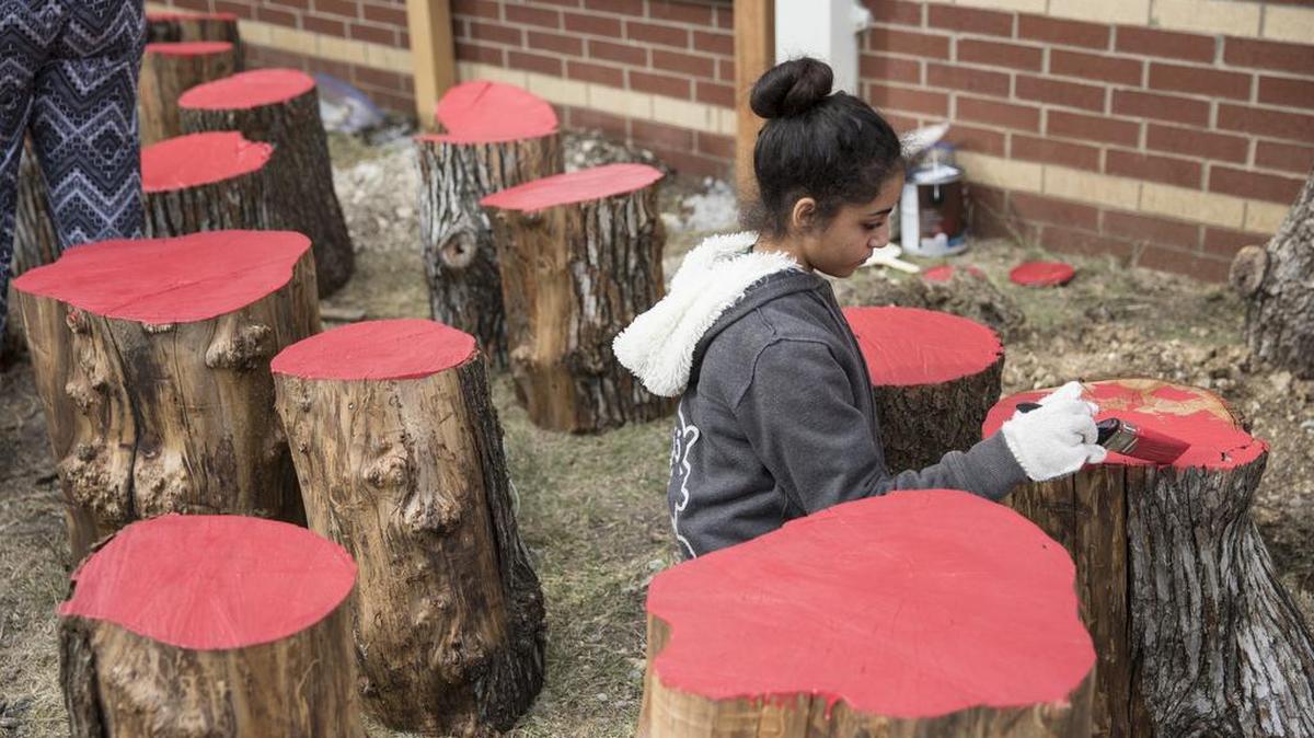 Rebecca Guirguis paints tree stump seats at the school on Saturday.