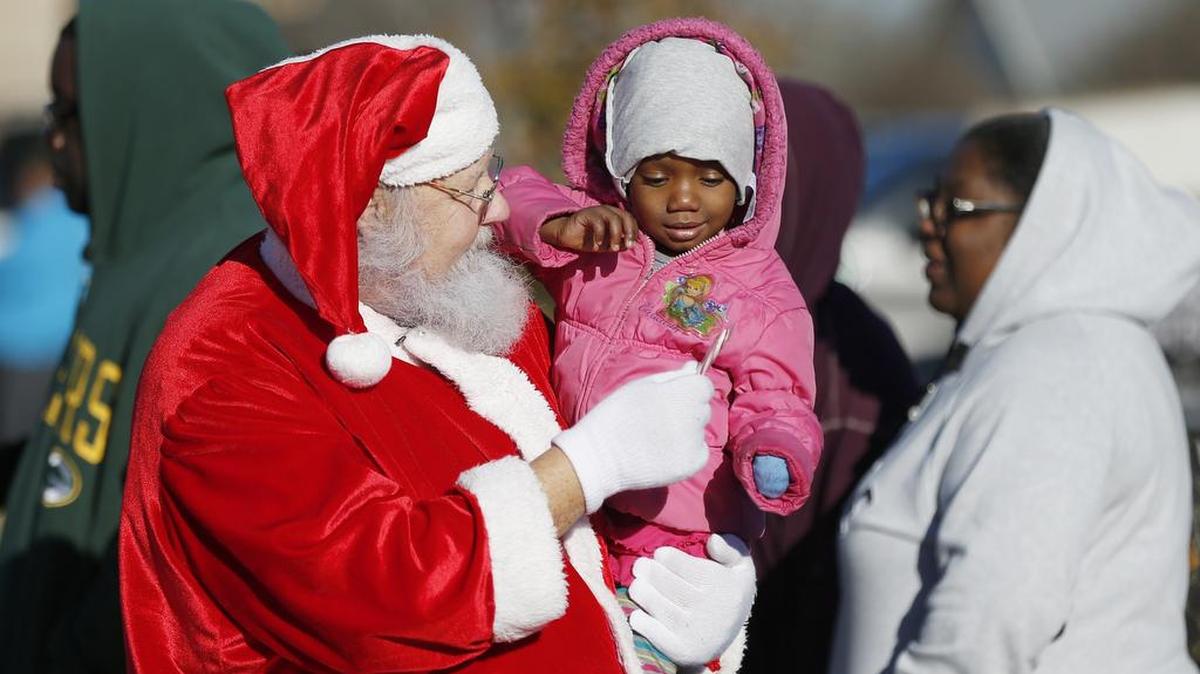 Santa Claus, also known as Roland Moore, hands Rose Smith, 2, a candy cane at a Christmas party at the Community Link food bank in Saginaw.