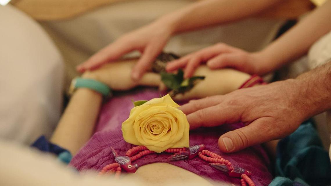 
LuAnn Denboer’s husband and daughters touch her during her home funeral service in June in Fort Worth.
