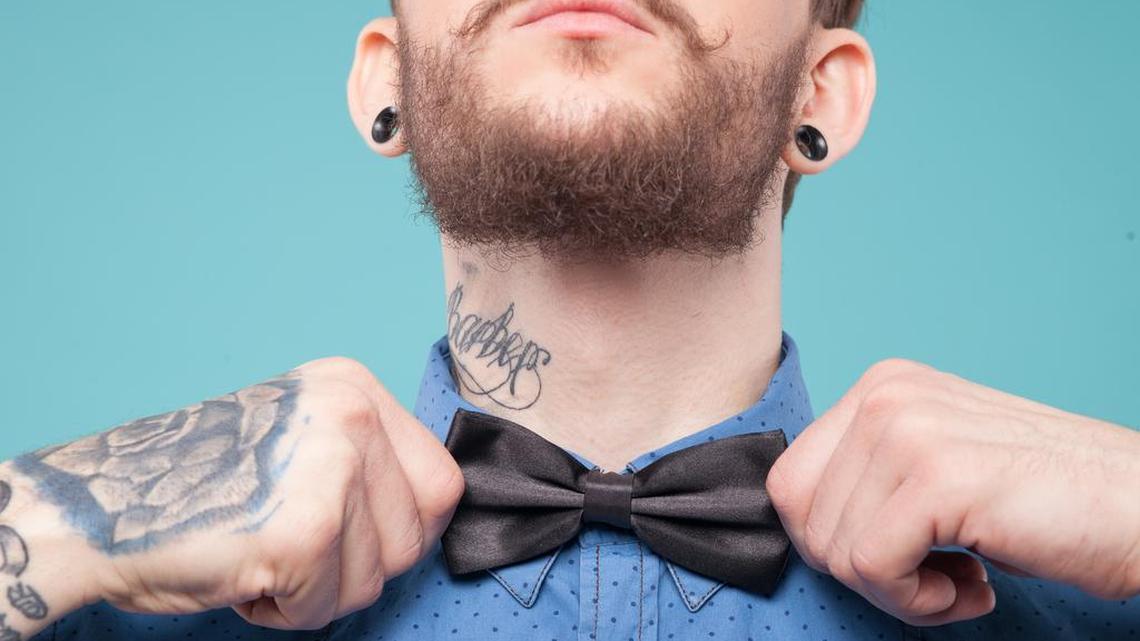 A man with a neck tattoo adjusts his tie.