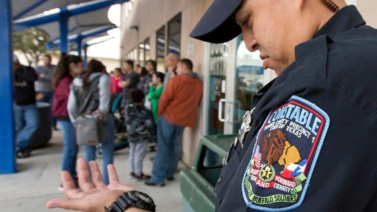 A Travis County constable checks the time outside the county passport office. The office opens at 8 a.m., but some families start lining up as early as 5 a.m.