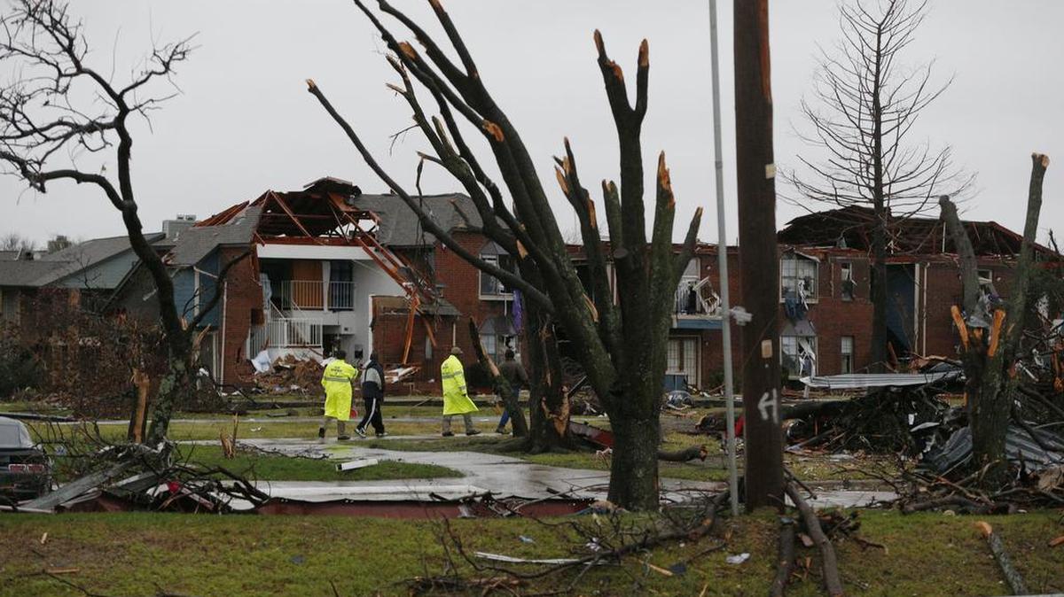 Residents and emergency workers walk near stripped trees Sunday at an apartment complex damaged by Saturday's tornado in Garland.