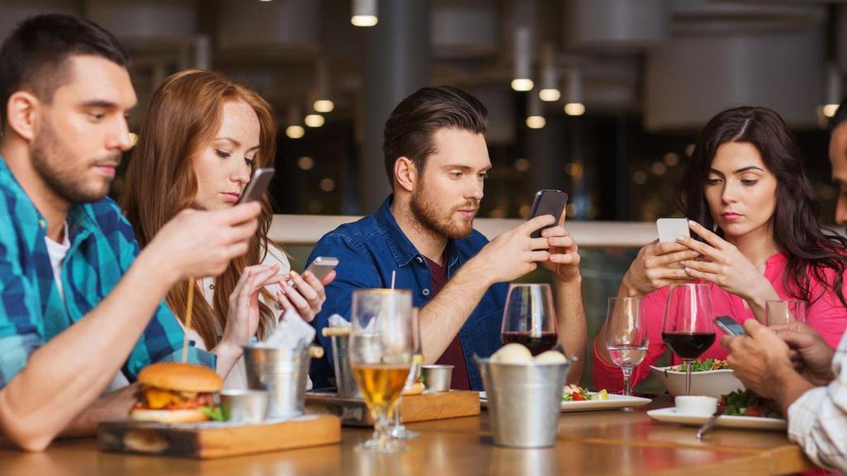 Friends with smartphones dining at restaurant.
