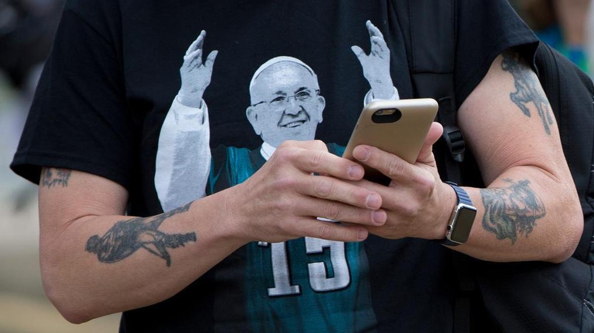 
A man wears an image of Pope Francis on his T-shirt while working his smartphone. 
