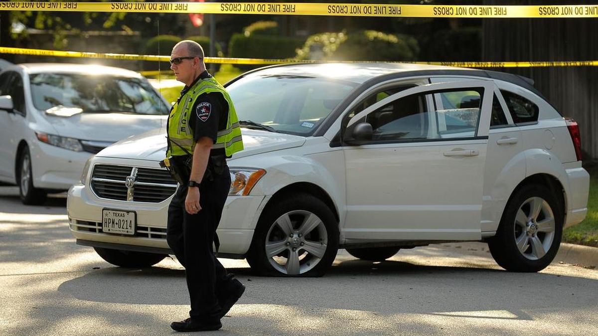 An Arlington policeman walks past the white Dodge sedan that a suspect car-jacked and abandoned near Shady Valley Drive in Arlington, TX, Saturday, July 15, 2017. A suspect car-jacked the car, lost control and fled on foot, carrying a weapon. The suspect, who was wearing a mask and body armor, was shot by police, says Lt. Christopher Cook.