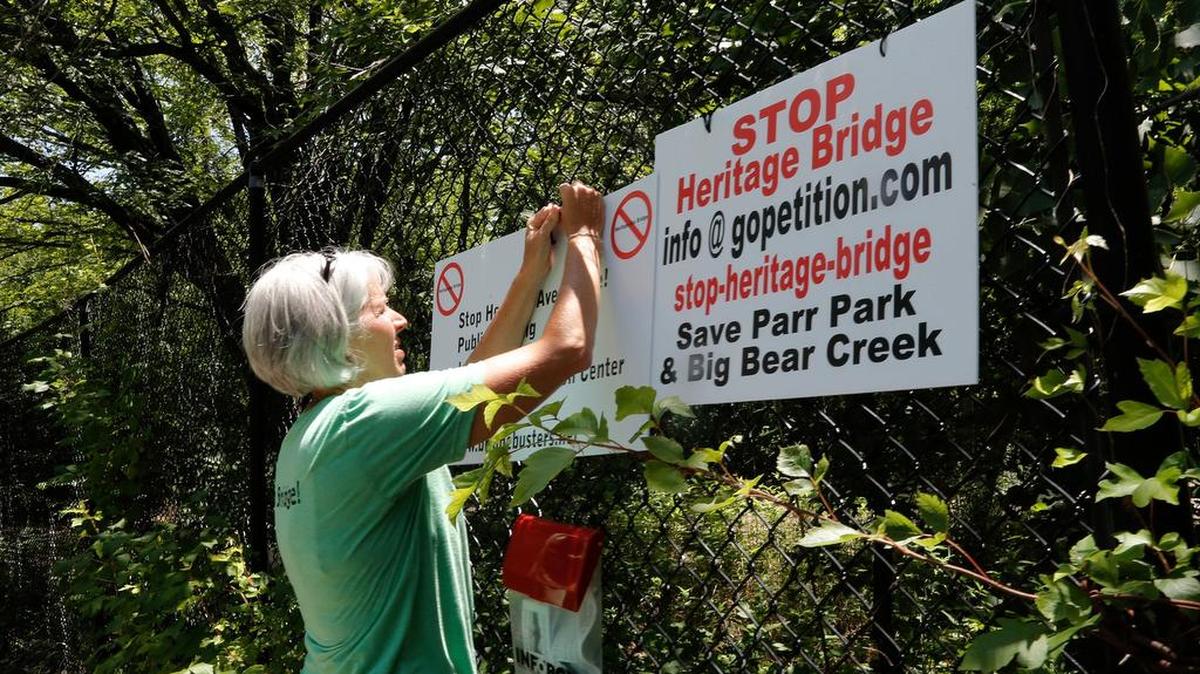 Dana McCormick posts a sign in Parr Park to inform neighbors that some residents oppose building a bridge linking Heritage Avenue, a proposal that is part of a bond package.