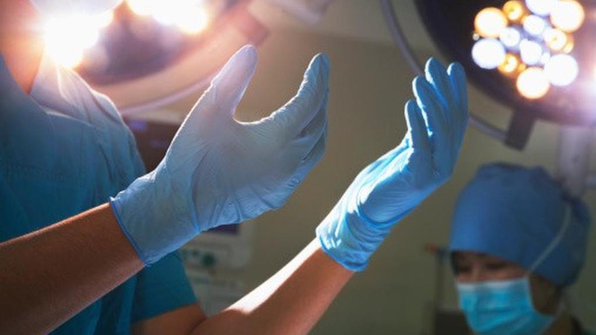Midsection view of hands in surgical gloves and lights.