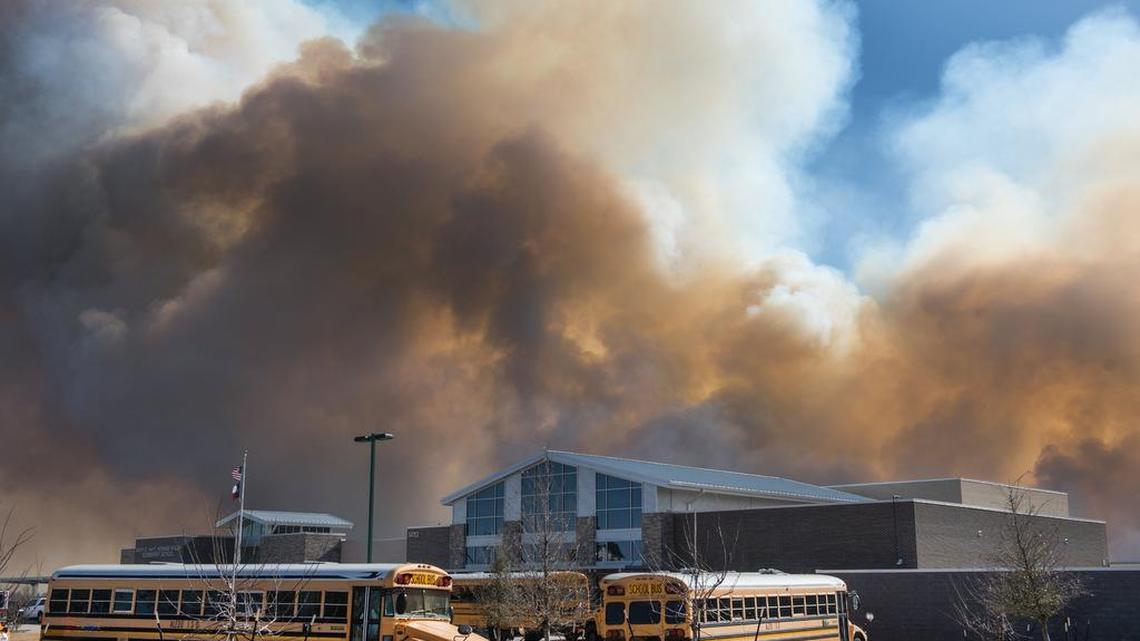 Buses lineup to evacuate students at the Walsh Elementary school on Monday as a large grass fire moves towards the building.