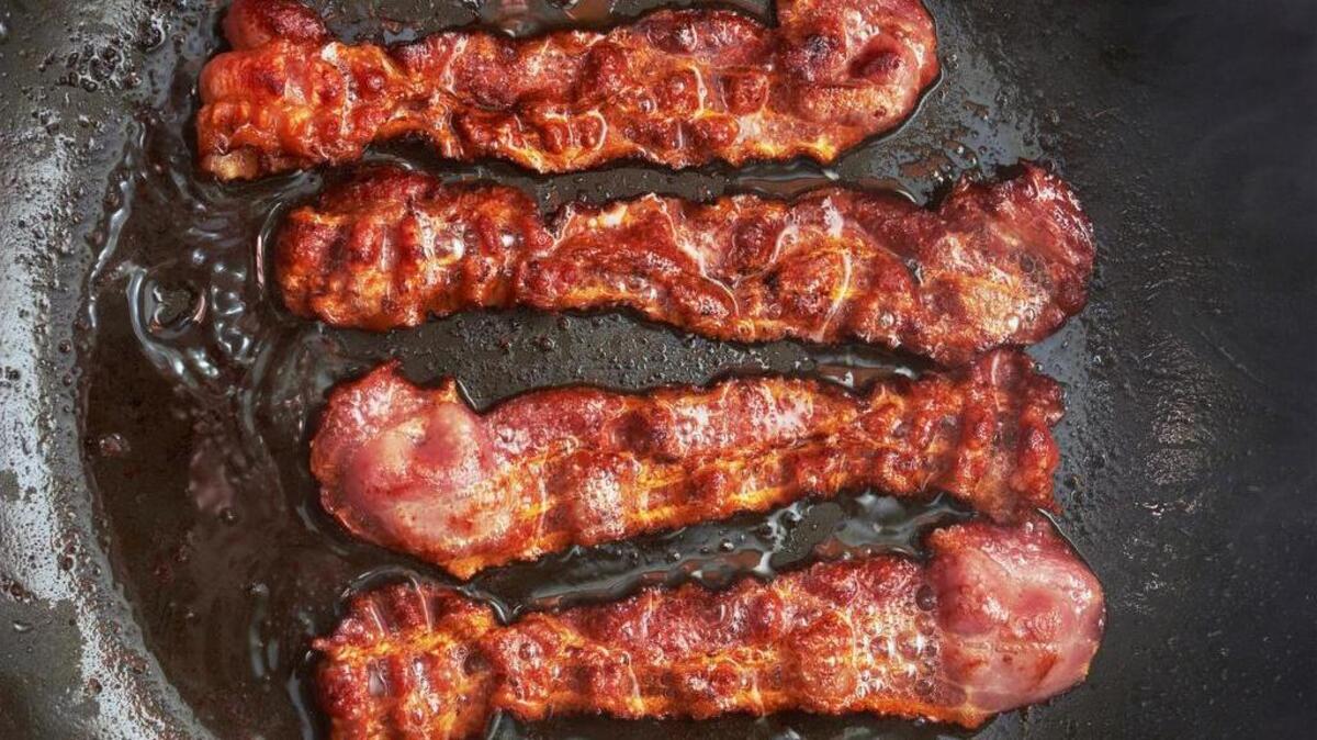 Slices of bacon sizzling in a frying pan