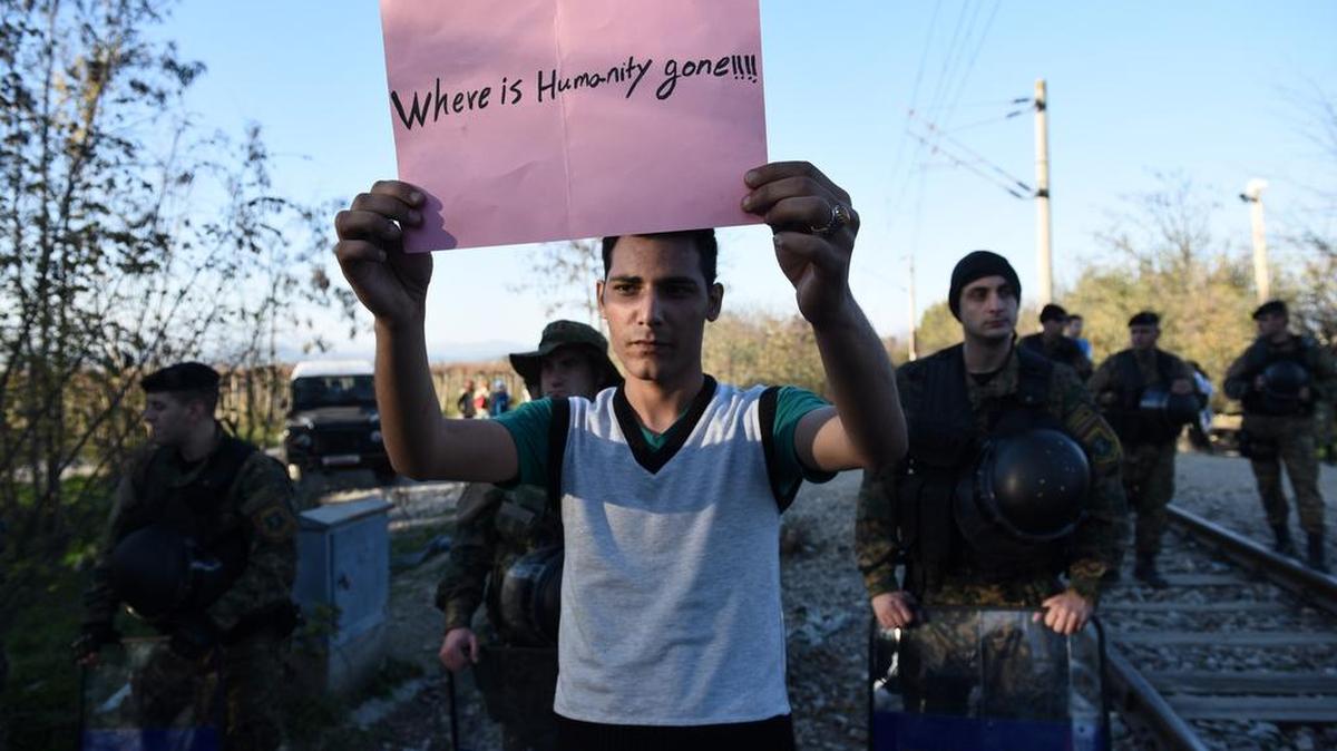 A migrant holds a sign in no-man’s land between Macedonia and Greece on Nov. 19.