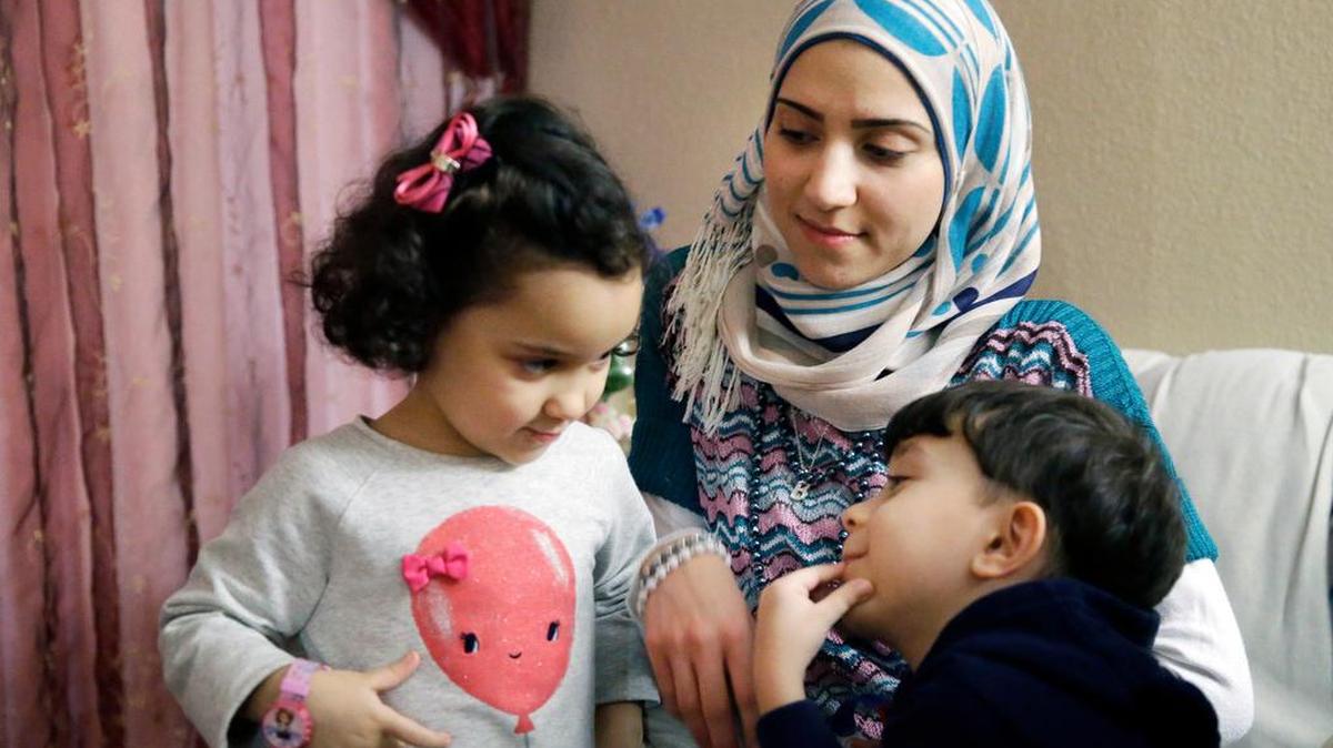 Syrian refugee Maryam al Jaddou, center, looks on as her children twins Maria, left, and Hasan, sit with her at their apartment in Dallas in November.
