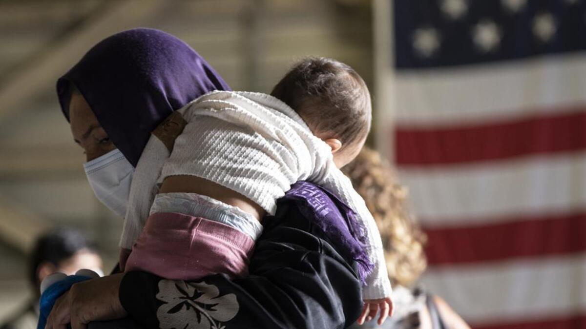 A woman holds a baby at the Sigonella NATO Airbase, Italy, Wednesday, Sept. 1, 2021. While a group of Afghan evacuees was boarding a plane headed to the US on Wednesday, children at the Sigonella NATO Airbase in Italy were walking around or playing with a ball patiently waiting for their turn to start a new life, just a few days after massive international airlift operations to evacuate locals at risk ended on Monday as the last American soldiers left Kabul airport.(AP Photo/Giuseppe Distefano)