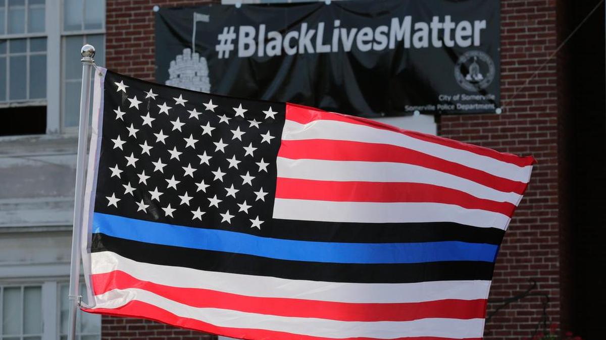 A United States flag, with blue and black stripes in support of law enforcement officers, flies at a protest by police and their supporters outside Somerville City Hall, Thursday, July 28, 2016, in Somerville, Mass. Somerville Mayor Joe Curtatone is promising not to remove a Black Lives Matter banner from City Hall despite complaints from police officers in the state.