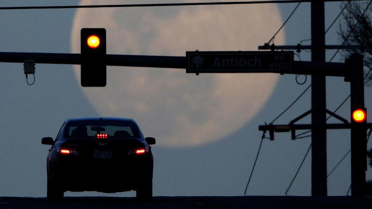 FILE - In this March 30, 2018, file photo, a motorist waits at a traffic light while the waxing full moon rises in the distance in Overland Park, Kan. The number of people killed by drivers running red lights has hit a 10-year high, and AAA is urging drivers and pedestrians to use caution at traffic signals. (AP Photo/Charlie Riedel, File)
