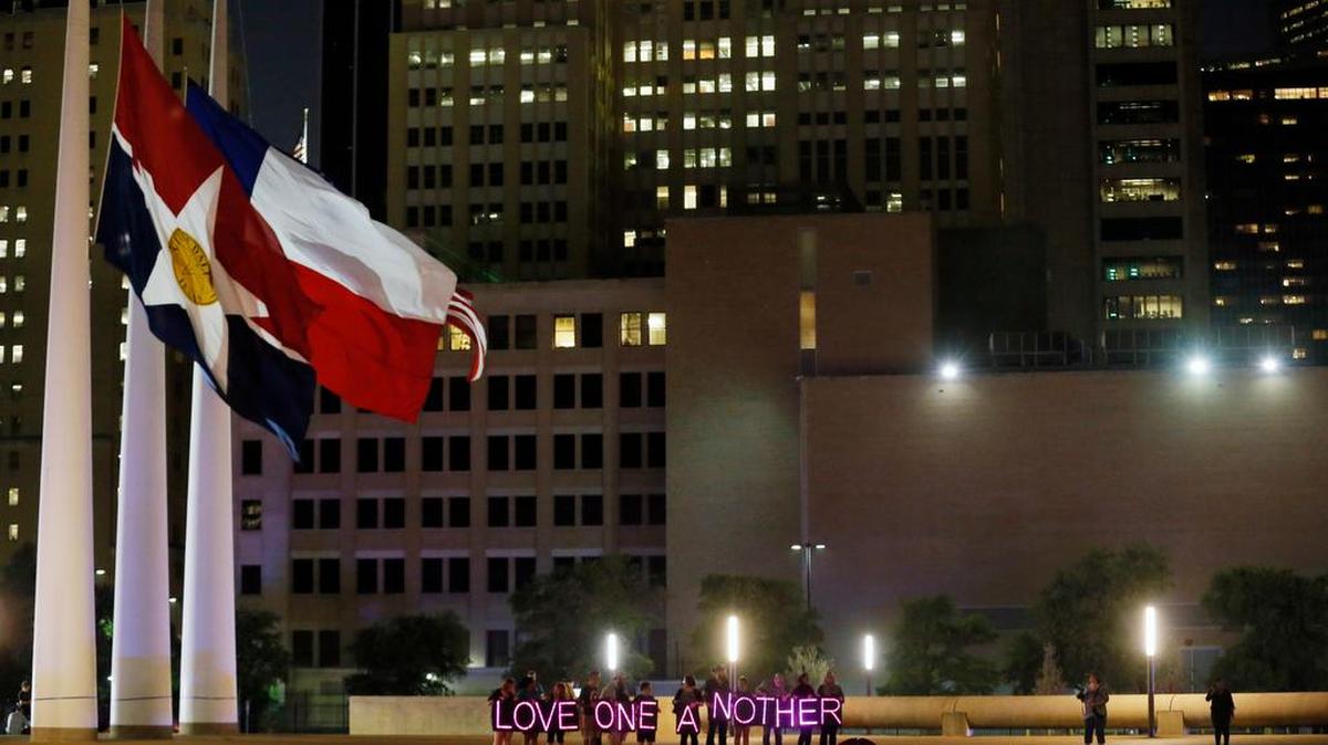 A group holds illuminated signs to spell out "Love One Another" under flags flying at half-f during a candlelight vigil at City Hall, Monday, July 11, 2016, in Dallas. Five police officers were killed and several injured during a shooting in downtown Dallas last Thursday night.