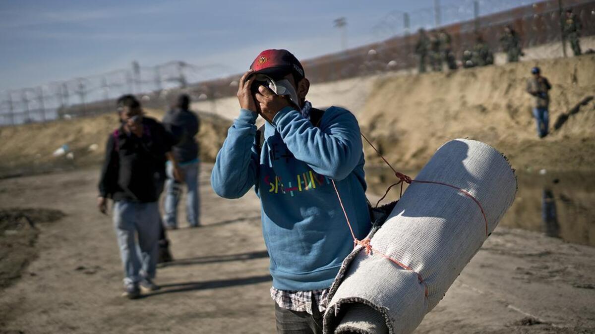 A migrant carrying a roll of carpet wipes his face after U.S. border agents fired tear gas at a group of migrants who had pushed past Mexican police at the Chaparral border crossing in Tijuana, Mexico, Sunday, Nov. 25, 2018.