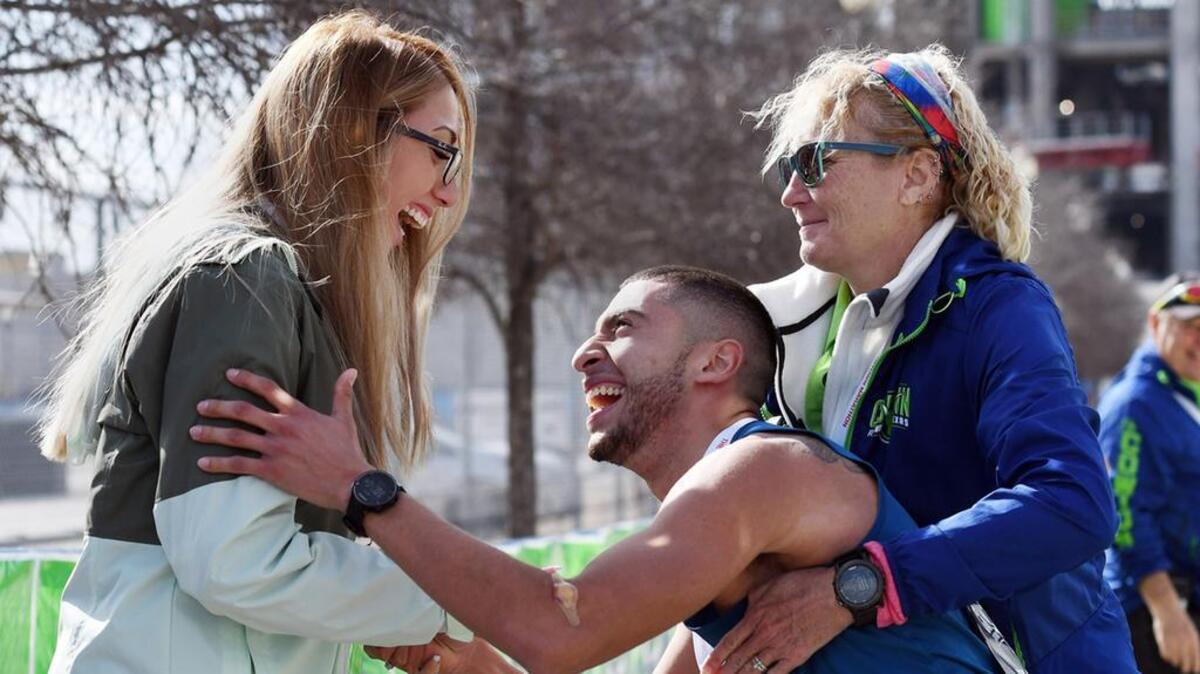 At the finish line, Gabriel Zambrano, center, gets some help to his feet from a race volunteer after proposing to Alyssa Rodriguez at the end of his completing the 2018 Cowtown Marathon.
