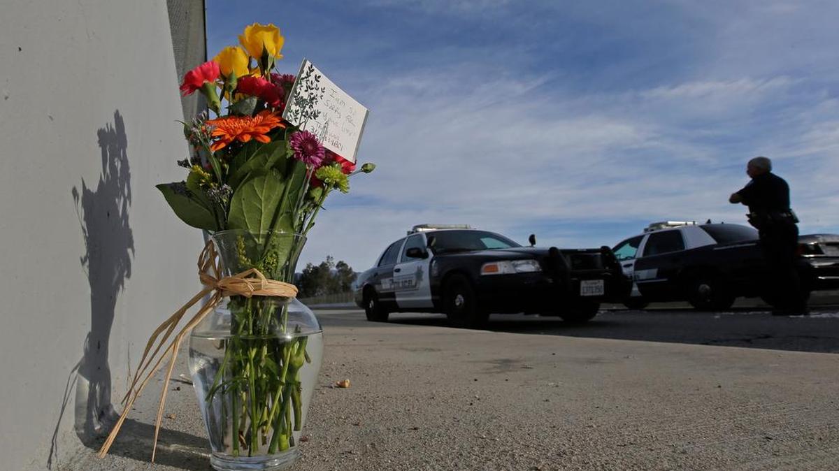 Flowers are left by the side of the road as a San Bernardino police officer blocks the road leading to the site of this week’s mass shooting in San Bernardino, Calif.