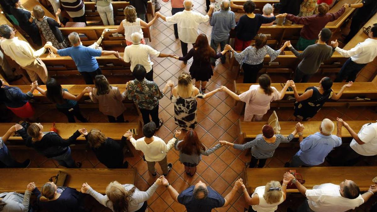 Churchgoers hold hands as they sing during a Sunday morning service at St. Pius X Church in El Paso, Texas, after more than 20 people were shot and killed at a local Walmart.