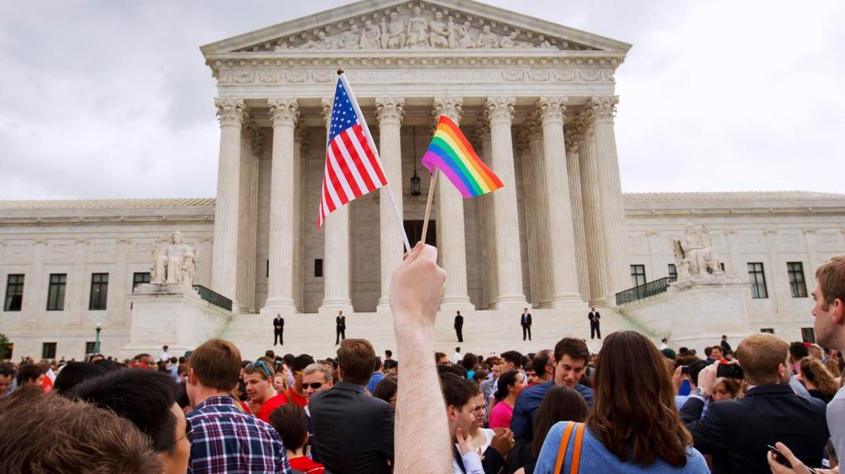In this Friday June 26, 2015, file photo, a man holds a U.S. and a rainbow flag outside the Supreme Court in Washington after the court legalized gay marriage nationwide. After the decision, religious conservatives are focusing on preserving their right to object. Their concerns are for the thousands of faith-based charities, colleges and hospitals that want to hire, fire, serve and set policy according to their religious beliefs, notably that gay relationships are morally wrong.