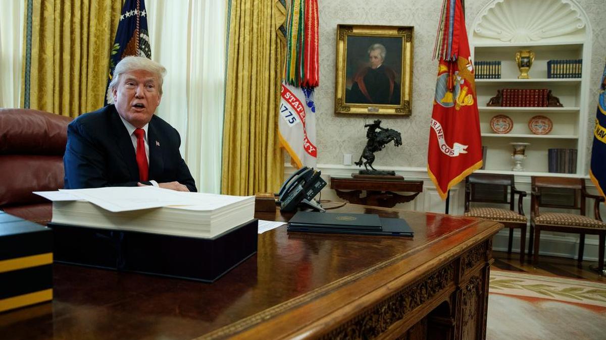 President Donald Trump speaks with reporters before signing the tax bill the Oval Office of the White House.