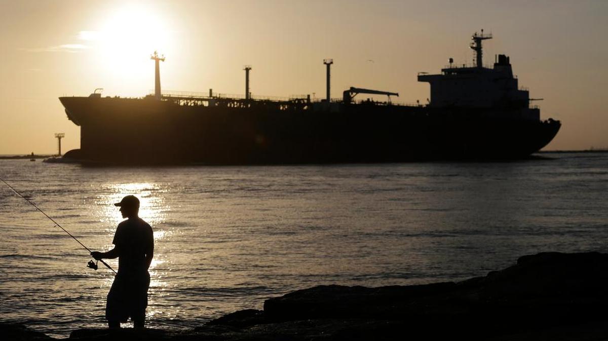 An oil tanker passes a fisherman as it enters a channel near Port Aransas, Texas, heading for Corpus Christi.