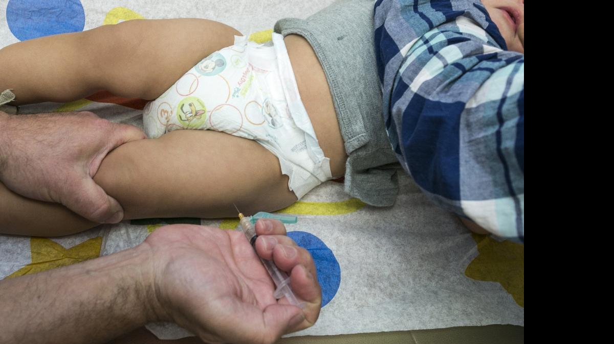 
A pediatrician uses a syringe to vaccinate a 1-year-old with the measles-mumps-rubella (MMR) vaccine. 
